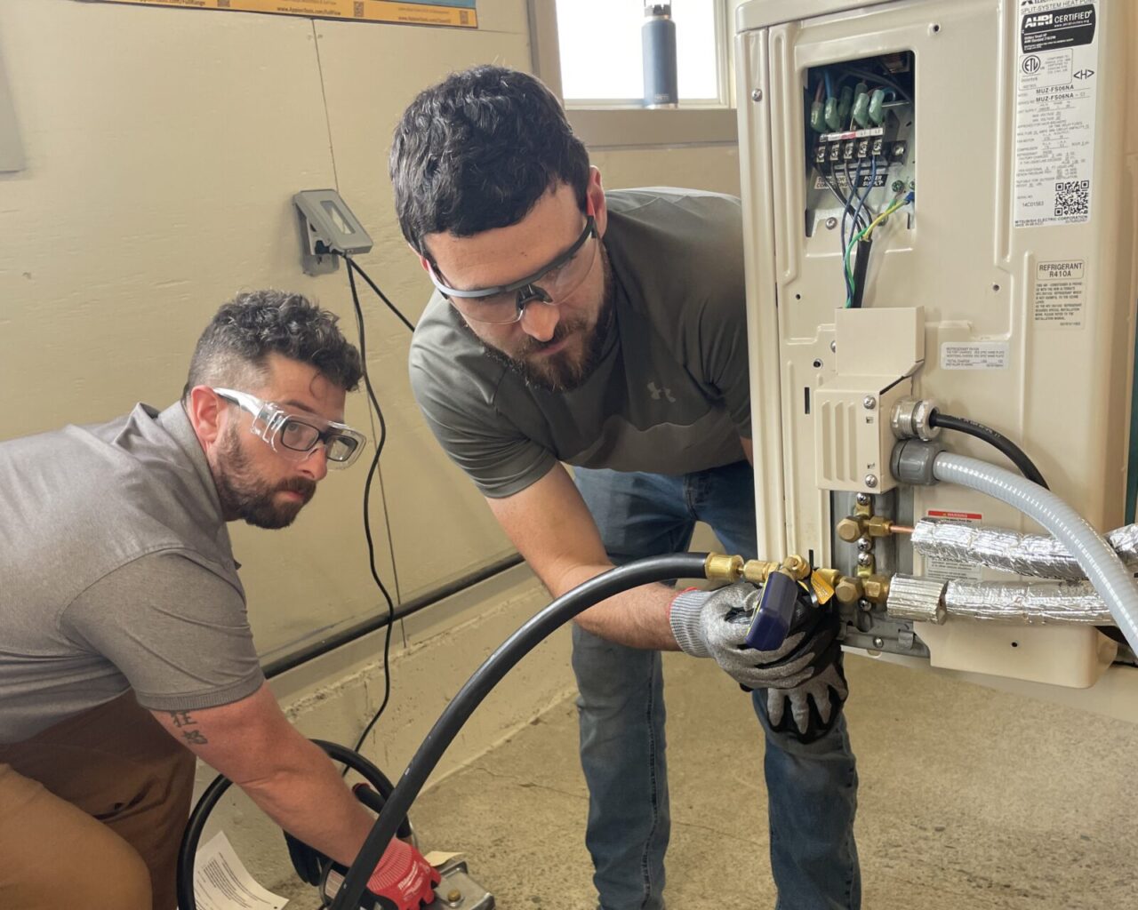 2 people using tools to work on a heat pump